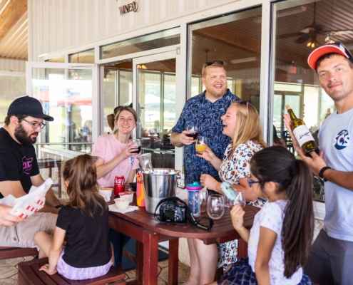 People share wine and conversation at an outdoor table at WSCW, enjoying a relaxed winery setting.